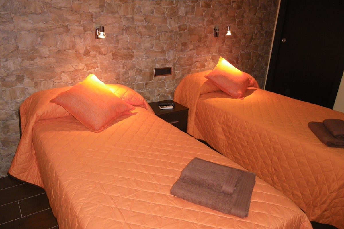 Two beds with orange bedding and pillows, a stone wall, and a door.