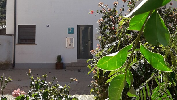 Un bâtiment blanc avec un toit recouvert de tuiles, une petite fenêtre et une porte. On y voit un panneau avec la lettre « P », qui indique un espace de stationnement.