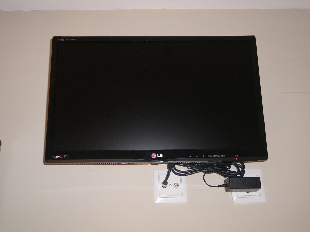 A flat-screen LG TV mounted on a wall with a power cord and adapter.
