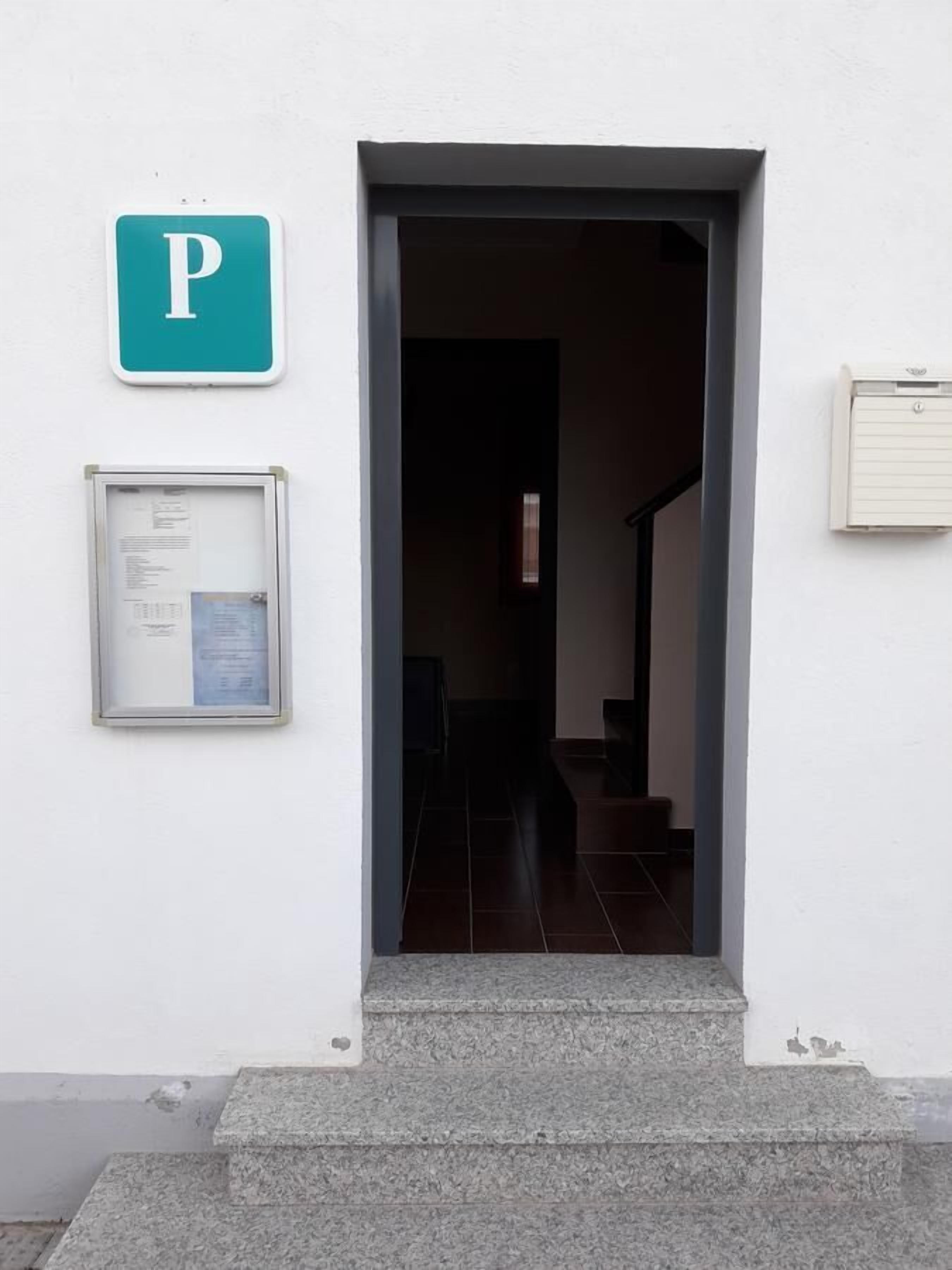 A building entrance with a parking sign, a notice board, and a small window.