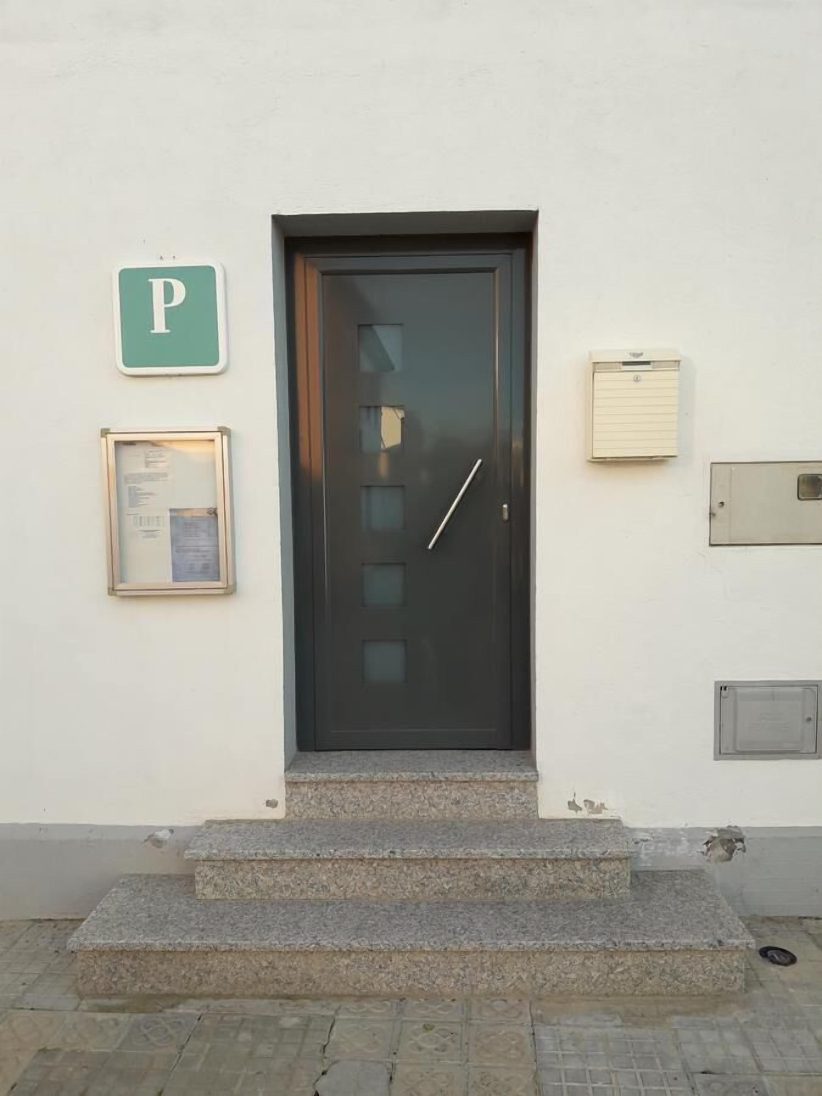 Eine schwarze Tür mit einem 'P'-Schild zur Kennzeichnung von Parkplätzen, einem Aushang und einer kleinen Stufe zum Eingang.