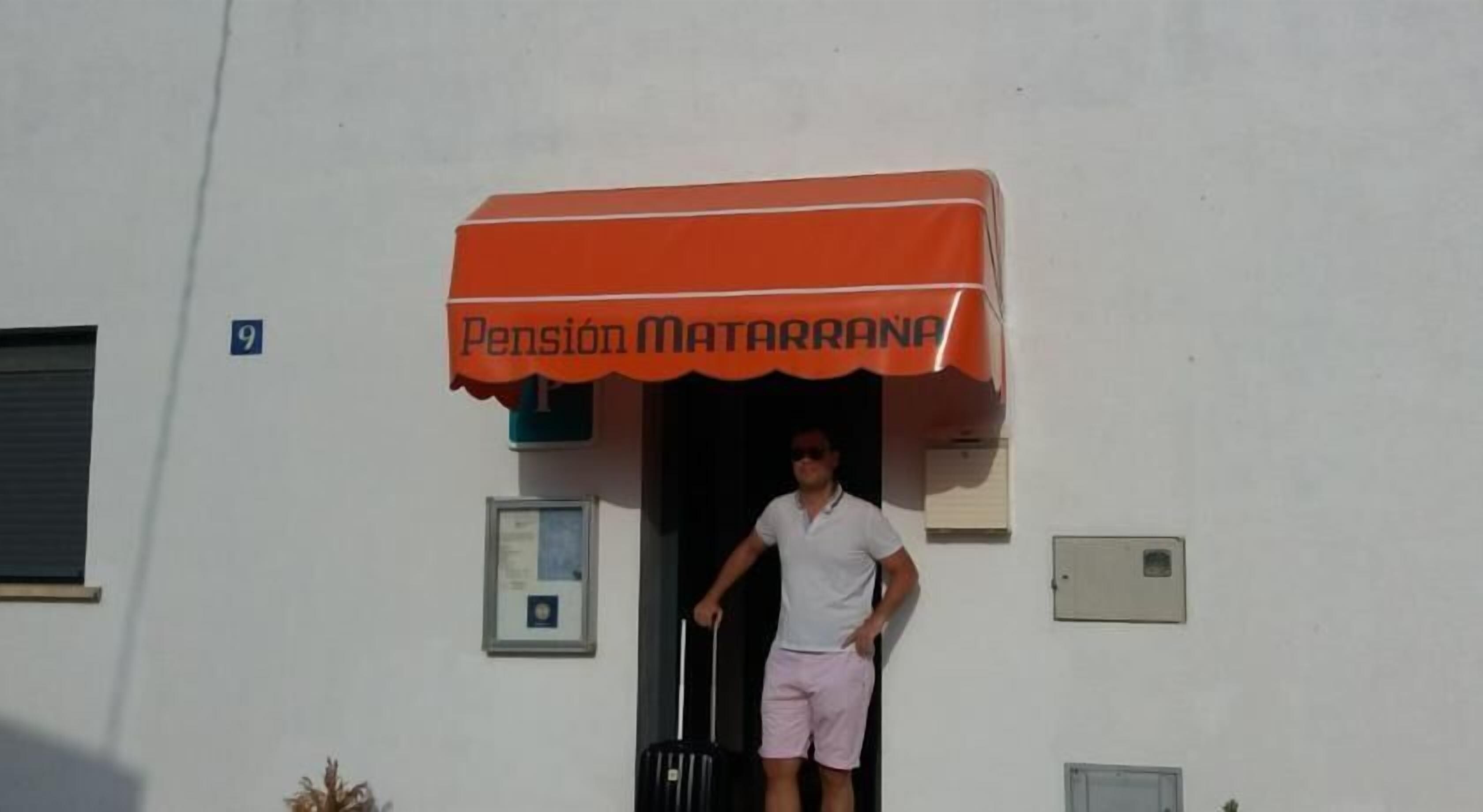 Un hombre sale de un edificio con un toldo naranja que dice 'Pension Matarrana'.