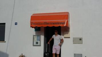 Un hombre sale de un edificio con un toldo naranja que dice 'Pension Matarrana'.