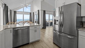 A modern kitchen with stainless steel appliances, a dining area with a view, and a ceiling fan. - 1661 - The Best Nest - Oceanfront Corolla | Pool, Putt-Putt & Hot Tub (Corolla)