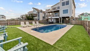 A modern two-story house with a backyard featuring a swimming pool, a wooden deck, and outdoor seating. - 1661 - The Best Nest - Oceanfront Corolla | Pool, Putt-Putt & Hot Tub (Corolla)