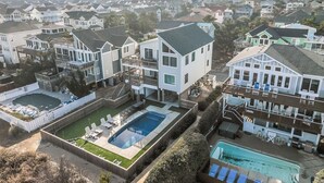 A residential area with multiple houses, a swimming pool, and a fenced yard. - 1661 - The Best Nest - Oceanfront Corolla | Pool, Putt-Putt & Hot Tub (Corolla)