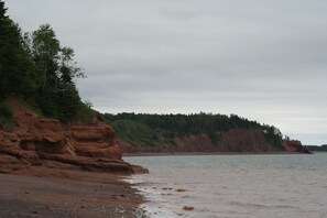 A coastal landscape with rocky cliffs and a beach. - Bay of Fundy ,Cobequid Bay, Steps to the beach in the Cliffs of Fundy Geopark (Economy)