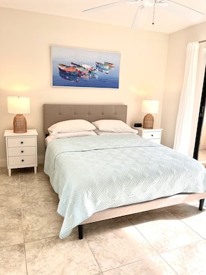 Ein Schlafzimmer mit einem Bett, zwei Nachttischen, einem Hocker und einem Wandbild mit Booten.