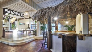 A spacious lobby with a thatched-roof bar area, tiled flooring, and a seating area with a view of the outdoors.