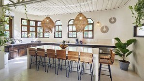 A spacious kitchen with a large island, wooden bar stools, and hanging rattan light fixtures.