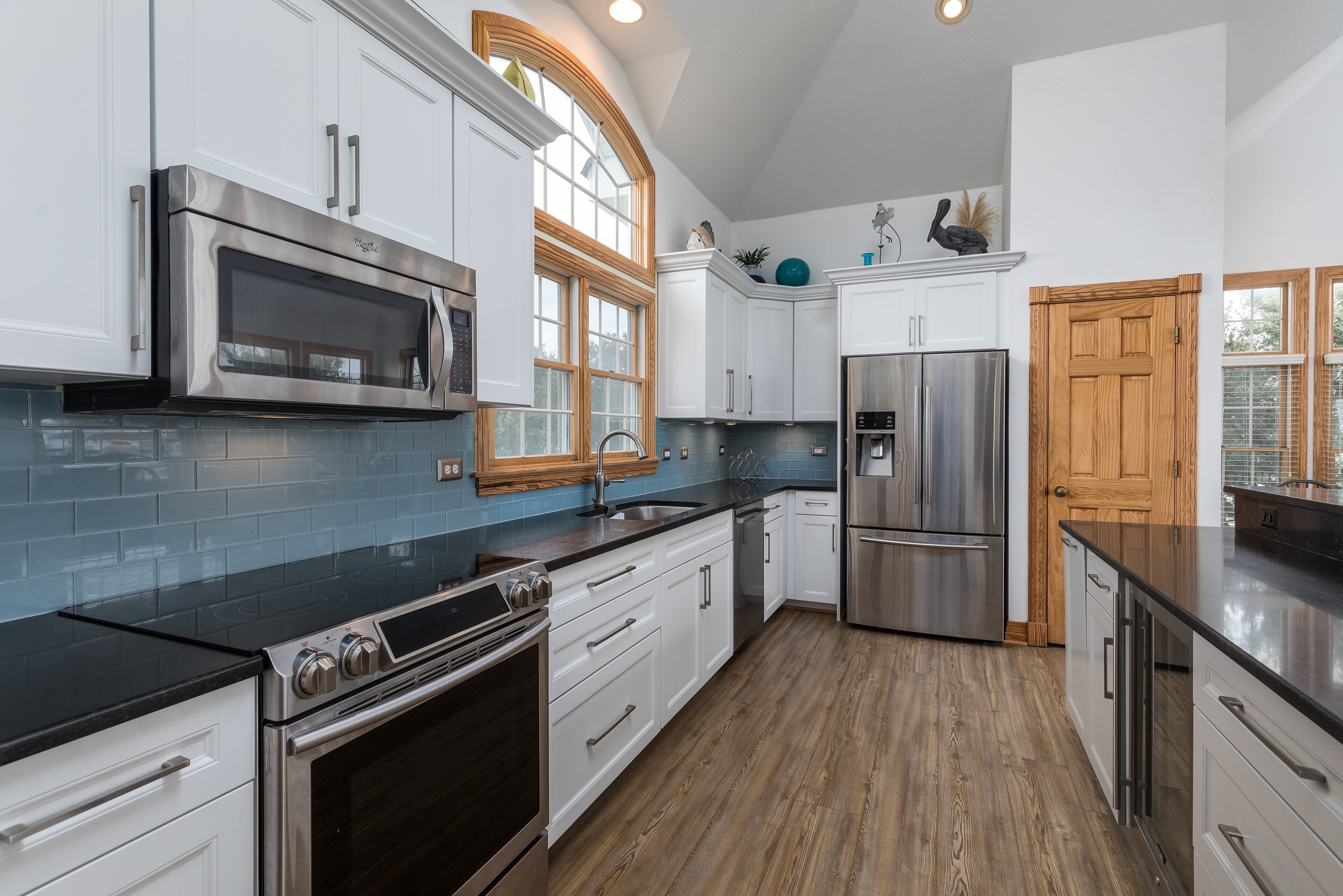 A modern kitchen with white cabinetry, stainless steel appliances, and a wooden floor.