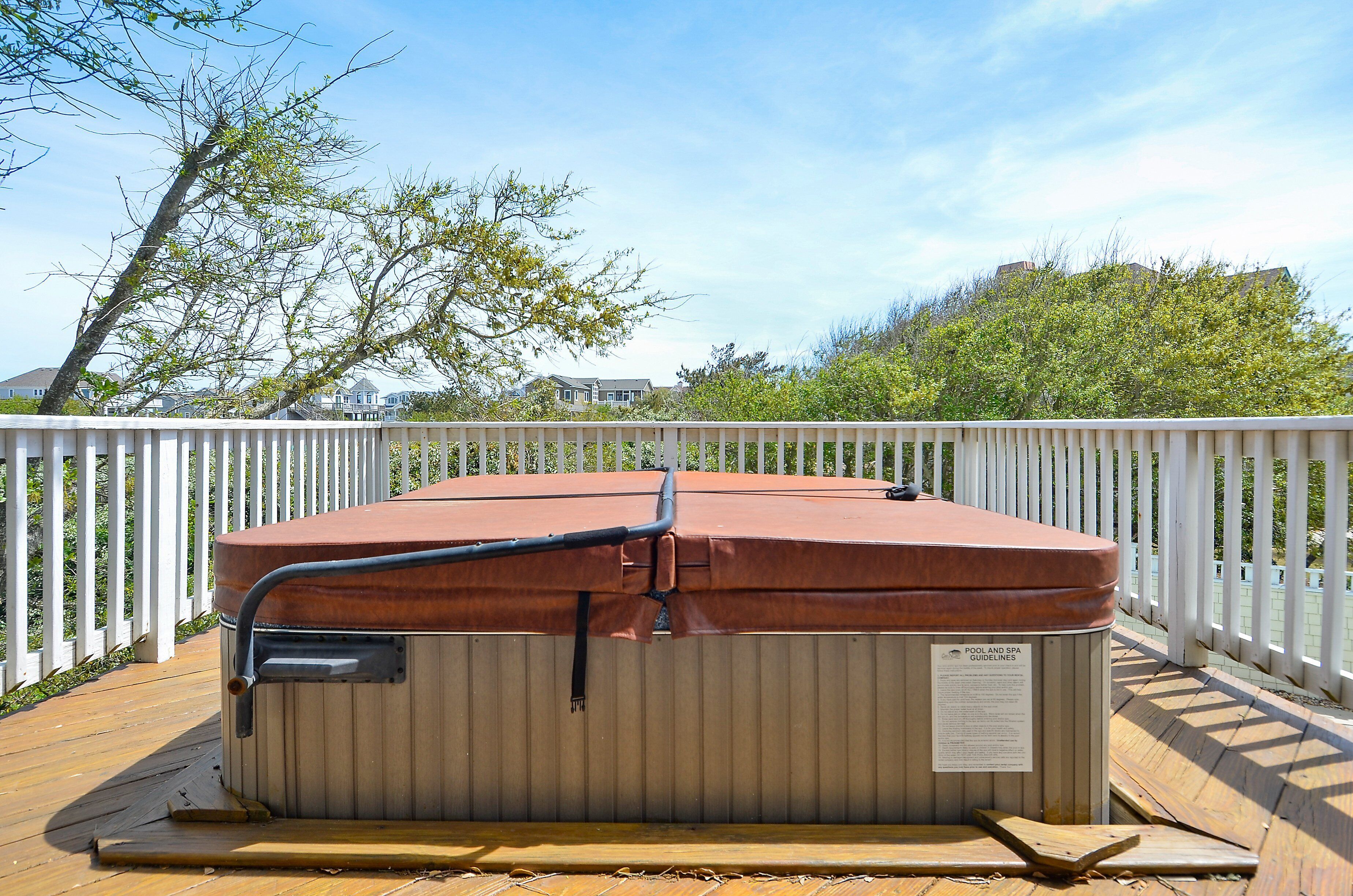 Un jacuzzi en una terraza de madera con una cerca blanca y árboles al fondo.