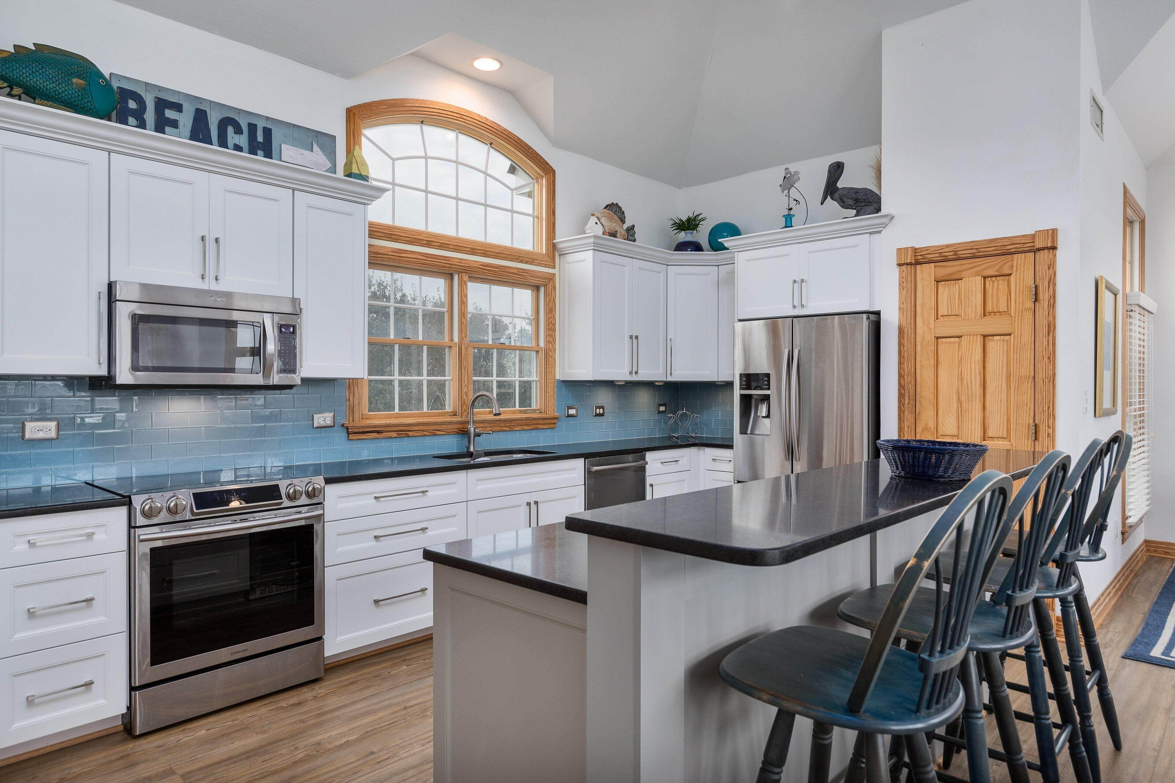 A modern kitchen with white cabinets, a stainless steel oven, a microwave, and a large window.