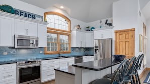 A modern kitchen with white cabinets, a stainless steel oven, a microwave, and a large window. - 2304 - High Spirits - Pine Island Retreat | Pool, Hot Tub, Near Beach (Corolla)