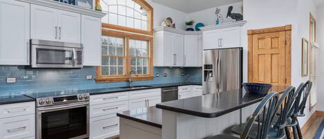 A modern kitchen with white cabinets, a stainless steel oven, a microwave, and a large window.