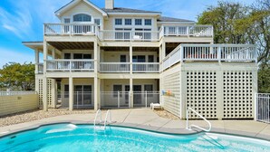 A two-story house with a swimming pool, multiple balconies, and a fenced backyard. - 2304 - High Spirits - Pine Island Retreat | Pool, Hot Tub, Near Beach (Corolla)