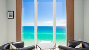 A room with a large sliding glass door leading to a beach view, two leather chairs, and a small table. - Awesome East Side Condo- Sea Forever (Navarre)