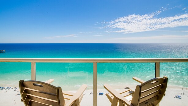 A balcony with two wooden chairs overlooking a beach with clear turquoise waters and a pier in the distance. - Awesome East Side Condo- Sea Forever (Navarre)