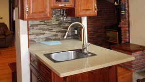 Una cucina con mobili in legno, un piano di lavoro in granito, un lavello in acciaio inossidabile e un camino in mattoni.