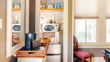 Cocina compacta equipada con microondas, refrigerador y estufa. Cuenta con una silla y una ventana con persianas.