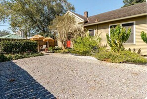 A house with a gravel driveway, a red door, and a covered outdoor seating area.