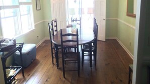 A dining room with a wooden table and chairs, a chandelier, and a view of the dining area through an open door.