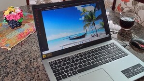 Una cocina con una laptop sobre una encimera de granito, una cafetera y cristalería de colores en la repisa.