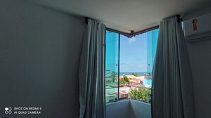 Una habitación con un ventanal grande, cortinas blancas y un equipo de aire acondicionado.