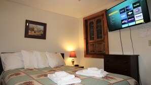 A hotel room with a bed, a television displaying streaming services, a framed picture on the wall, and a lamp. - Cooperstown Baseball Rentals - Lakeview Pines (Maryland)