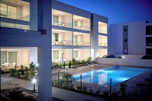 A modern hotel with a rooftop pool, multiple balconies, and outdoor seating areas.