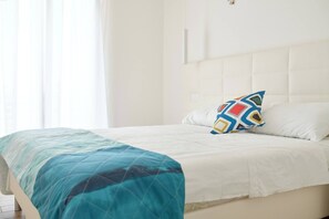 A neatly made bed with a white headboard, a teal blanket, and a colorful pillow. - West Village Appartamento - NUOVO con piscina (Jesolo)