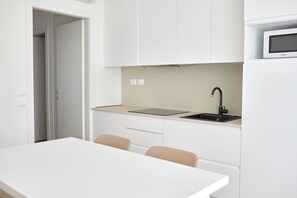 A modern kitchen with white cabinets, a black faucet, and a microwave on the countertop.
