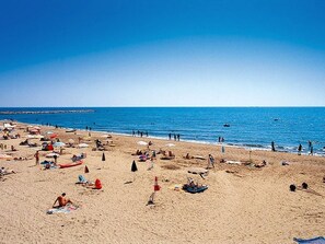 A beach with people sunbathing and swimming, umbrellas, and beach chairs.