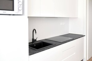 A modern kitchen with white cabinets, a black sink, and a black countertop. - West Village Appartamento - NUOVO con piscina (Jesolo)