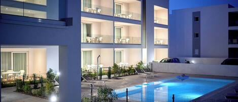 A modern hotel with a rooftop pool, multiple balconies, and outdoor seating areas.