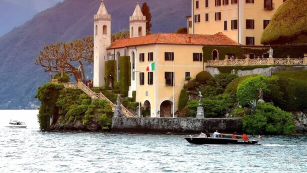 A historic building with two towers, a flag, and a boat in the foreground.