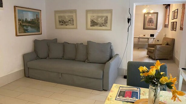 A living room with a grey sofa, a small table with a vase of flowers, and three framed pictures on the wall. - Ca' Molin, view on the Venetian canals (Venezia)