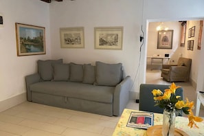 A living room with a grey sofa, a small table with a vase of flowers, and three framed pictures on the wall. - Ca' Molin, view on the Venetian canals (Venezia)