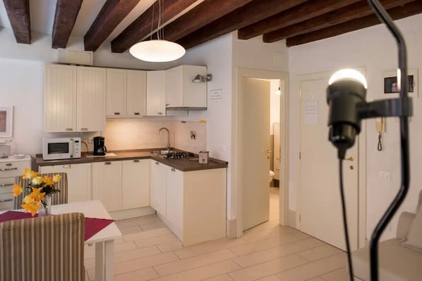 A compact kitchen with white cabinets, a microwave, a coffee maker, and a sink. There is a dining area with a table and chairs, and a vase with flowers. - Ca' Molin, view on the Venetian canals (Venezia)