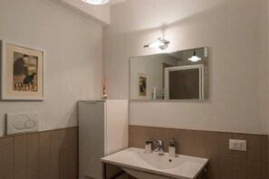 Une salle de bain avec un lavabo blanc, un miroir et un luminaire fixé au mur.