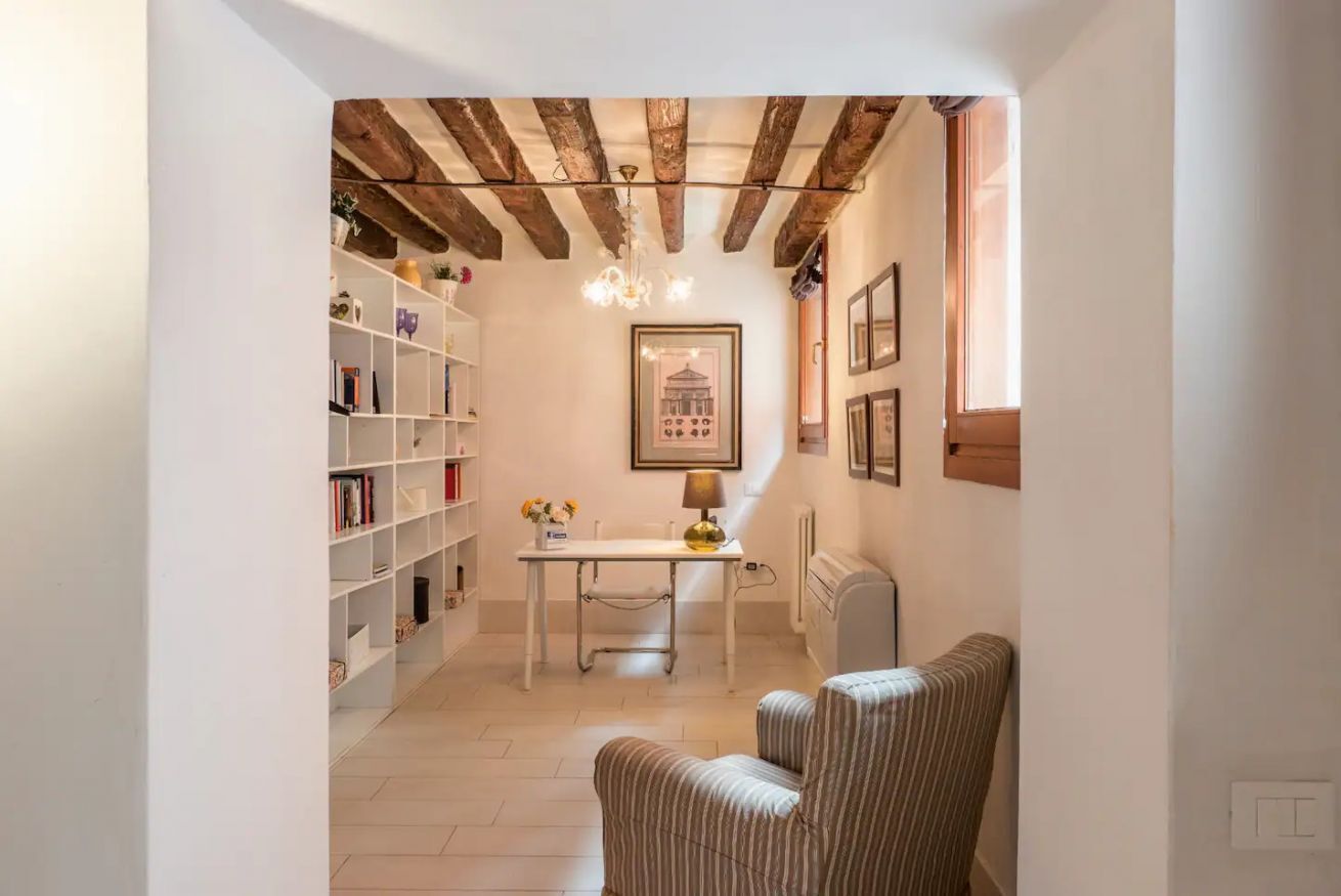 Un couloir étroit avec une bibliothèque blanche, une table avec une lampe et une chaise.