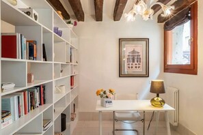 A room with white shelving units filled with books and decorative items, a white table with a lamp, and a framed picture on the wall. - Ca' Molin, view on the Venetian canals (Venezia)