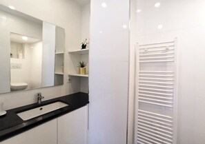 A modern bathroom with a black sink, white cabinets, a large mirror, and a white towel rack.