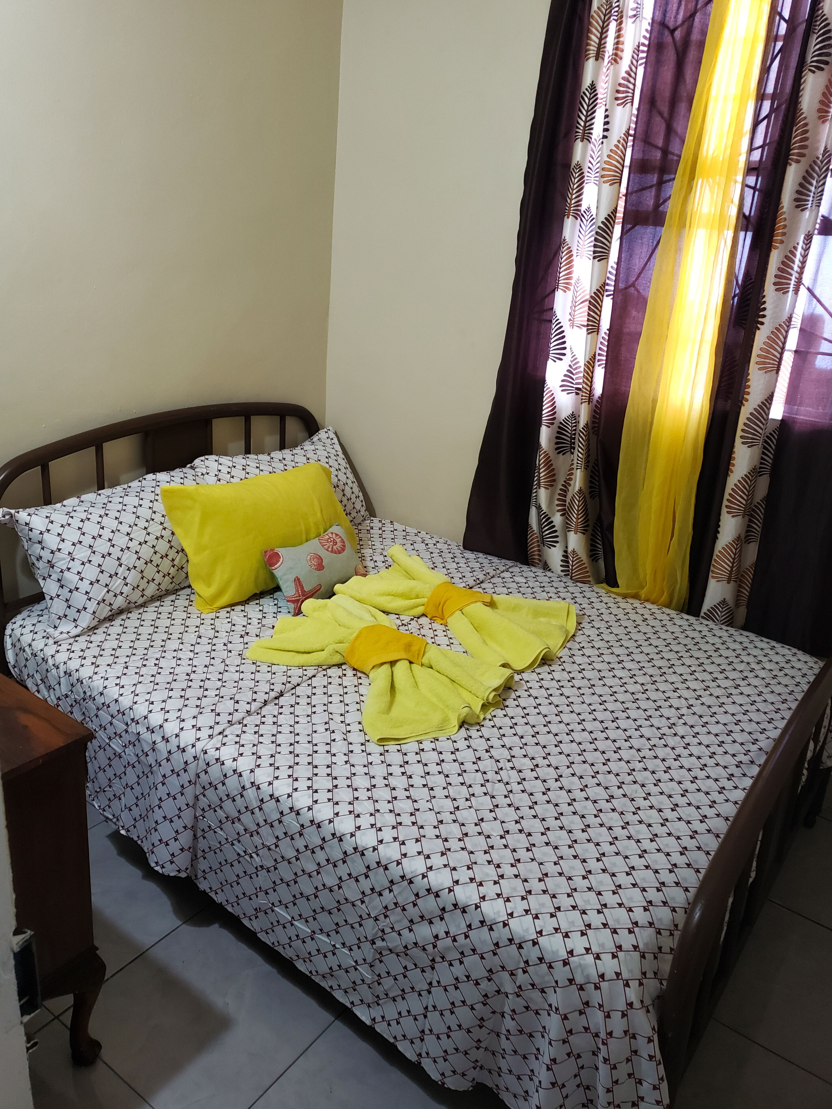 A bed with a patterned bedspread, a yellow pillow, and a yellow towel folded on the bed.