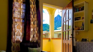 Sala de estar com sofá, mesa de centro e estante. Porta dá acesso a área externa com vista para as montanhas.