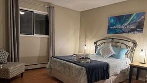 Ein Schlafzimmer mit einem Bett, einem Sessel, einem Nachttisch und einem Bild an der Wand.