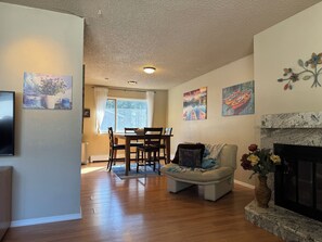 A living room with a fireplace, a dining area with a table and chairs, and artwork on the walls. - Granite Getaway - Quiet, Comfortable Place Offering 10% OFF ON TOURS! (Juneau)