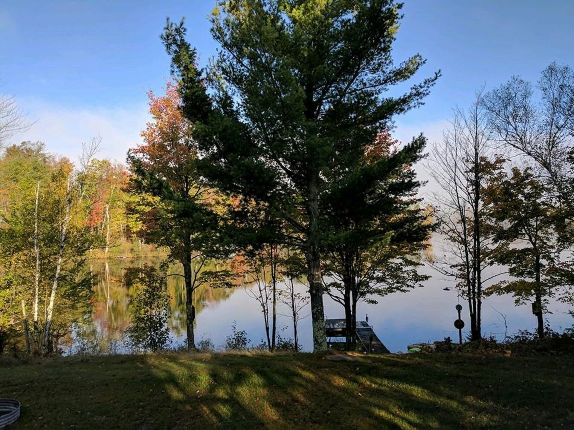 Un chalet au bord du lac, doté d’un quai, entouré d’arbres et offrant une vue sur un ciel dégagé.