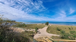 A beach with a wooden boardwalk leading to the shore, surrounded by grassy dunes and sparse vegetation. - New Buffalo home prime Location Hot tub Firepit Walk to All (New Buffalo)