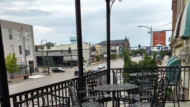 A covered outdoor seating area with metal tables and chairs, overlooking a street with buildings and a traffic light. - Great Apartment in Historic Downtown Columbus. (Columbus)